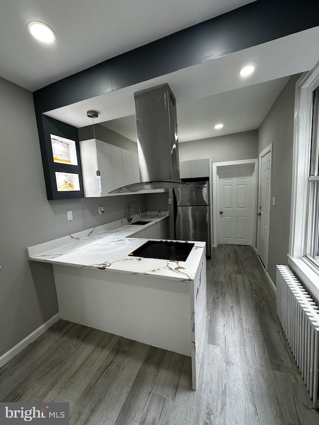 kitchen with island range hood, a peninsula, wood finished floors, freestanding refrigerator, and radiator