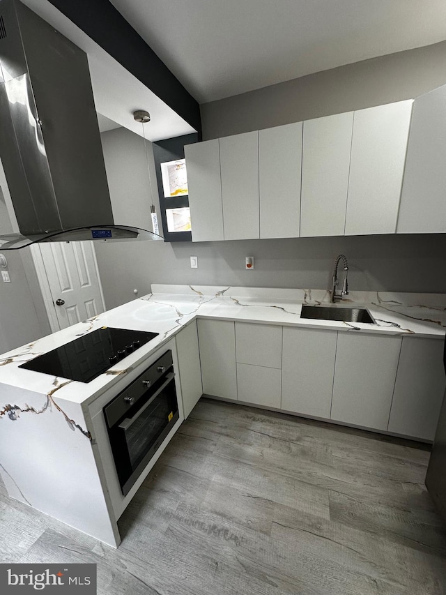 kitchen featuring black electric stovetop, extractor fan, oven, a sink, and light wood finished floors