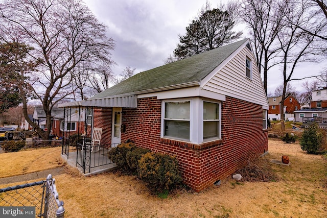 bungalow featuring brick siding, roof with shingles, a front yard, and fence