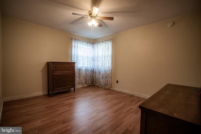 interior space with a ceiling fan, baseboards, and wood finished floors