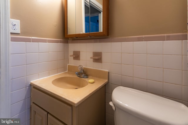 bathroom with toilet, vanity, and tile walls