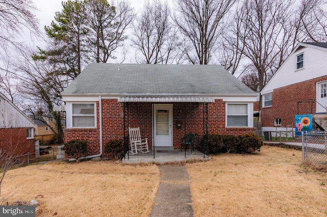 bungalow featuring a shingled roof, fence, a front lawn, and brick siding