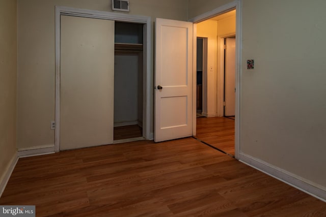 unfurnished bedroom with a closet, wood finished floors, visible vents, and baseboards