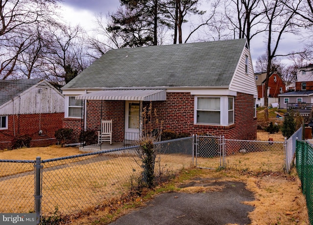 view of front facade featuring a fenced front yard, a gate, roof with shingles, and brick siding