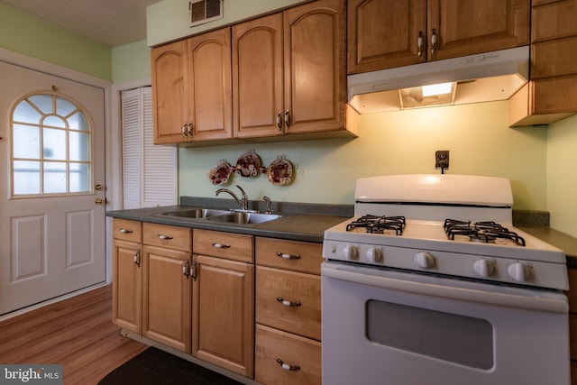 kitchen with white gas range oven, visible vents, dark countertops, under cabinet range hood, and a sink