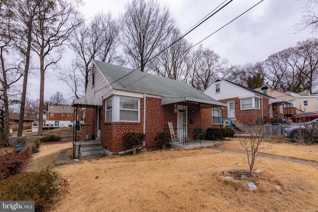 bungalow-style house with roof with shingles, fence, and brick siding