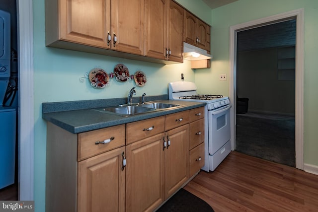 kitchen featuring dark wood-style flooring, white gas range, a sink, stacked washing maching and dryer, and under cabinet range hood