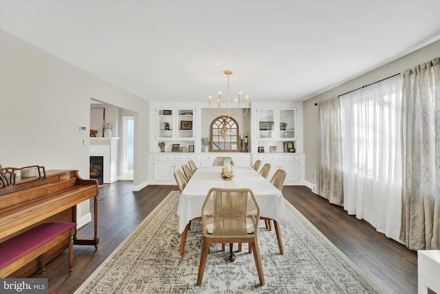 dining space with a notable chandelier, dark wood-type flooring, baseboards, and a glass covered fireplace