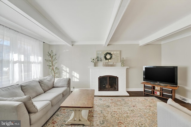 living area featuring wood finished floors, baseboards, visible vents, a fireplace, and beamed ceiling