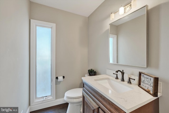 half bath with vanity, toilet, wood finished floors, and baseboards