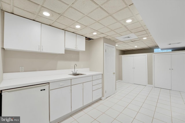 kitchen with a sink, light countertops, white cabinets, a paneled ceiling, and dishwasher