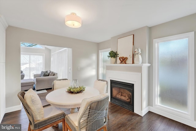 dining space featuring dark wood finished floors, a glass covered fireplace, and baseboards