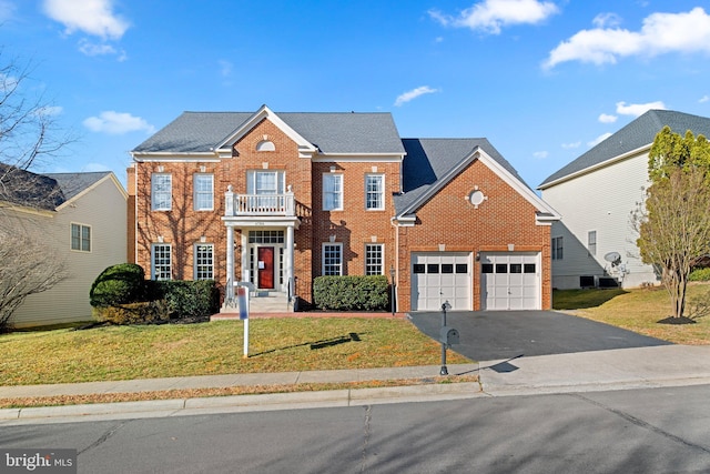 colonial-style house featuring a balcony, a garage, brick siding, driveway, and a front yard