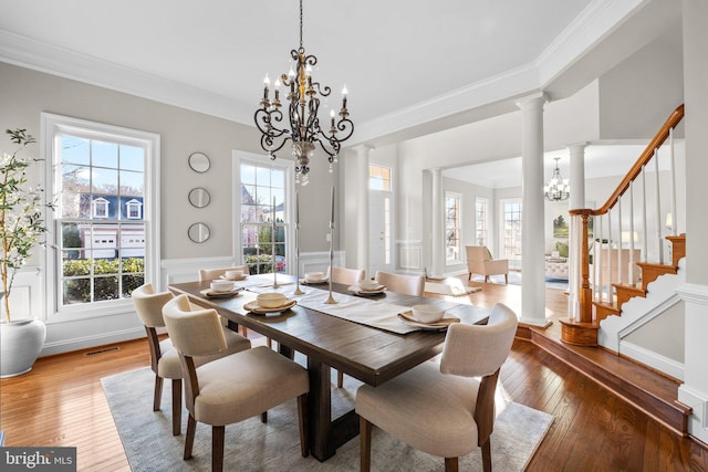 dining space featuring decorative columns, plenty of natural light, hardwood / wood-style flooring, an inviting chandelier, and stairs