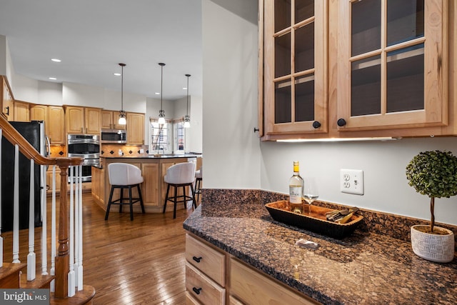 kitchen featuring glass insert cabinets, a kitchen breakfast bar, dark wood-style flooring, stainless steel appliances, and light brown cabinetry