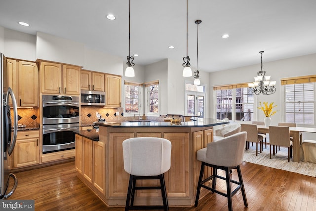 kitchen with stainless steel appliances, a kitchen island, dark wood finished floors, tasteful backsplash, and a kitchen bar