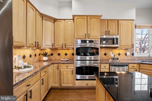 kitchen with stainless steel appliances, a sink, dark stone countertops, and light brown cabinetry