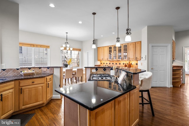 kitchen with tasteful backsplash, dark wood finished floors, glass insert cabinets, a kitchen breakfast bar, and stainless steel gas stovetop