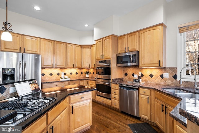 kitchen with dark wood-style floors, pendant lighting, appliances with stainless steel finishes, a sink, and dark stone counters