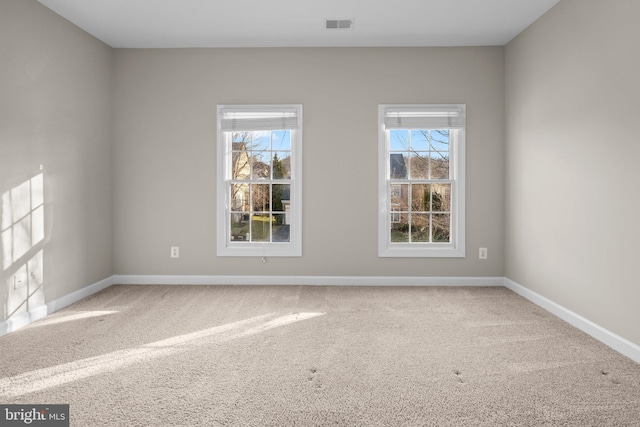 carpeted empty room featuring a healthy amount of sunlight, visible vents, and baseboards