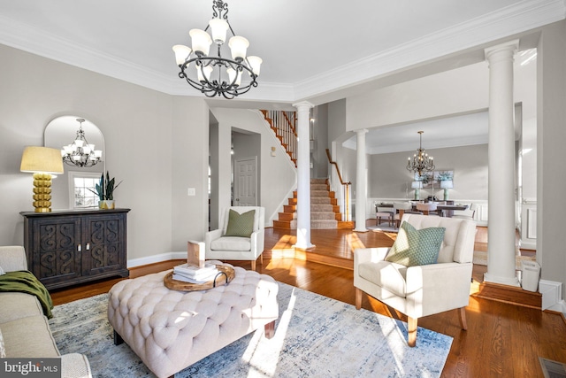 living area with stairway, ornamental molding, wood finished floors, an inviting chandelier, and ornate columns