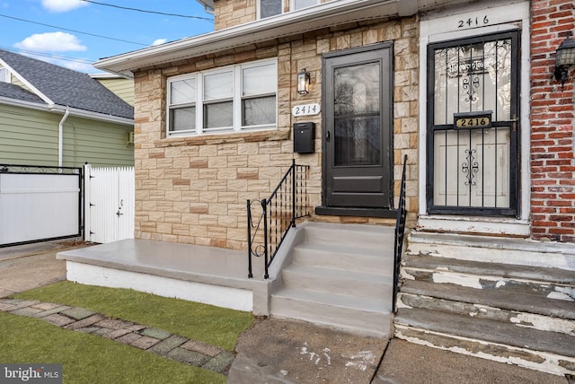 doorway to property with stone siding and fence