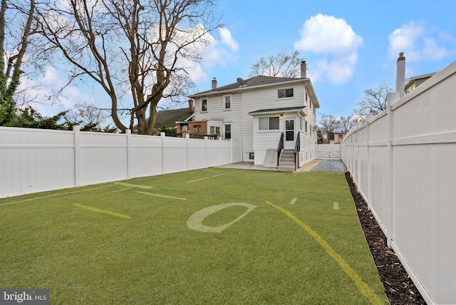 rear view of house featuring entry steps, a fenced backyard, a chimney, and a lawn