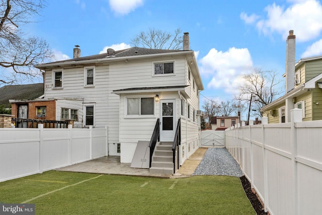 rear view of property with entry steps, a fenced backyard, a lawn, a chimney, and a patio area