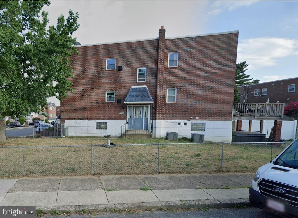 view of front facade with a fenced front yard, a front lawn, cooling unit, and brick siding