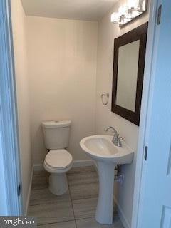 half bathroom with tile patterned flooring, toilet, baseboards, and a sink