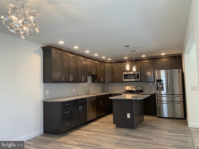 kitchen featuring light wood finished floors, a sink, decorative backsplash, dark brown cabinetry, and appliances with stainless steel finishes