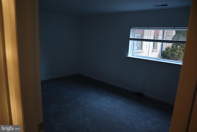 spare room with dark colored carpet, visible vents, and baseboards