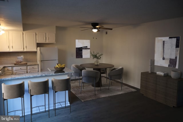 kitchen featuring tasteful backsplash, a kitchen breakfast bar, freestanding refrigerator, white cabinets, and dark wood-style flooring