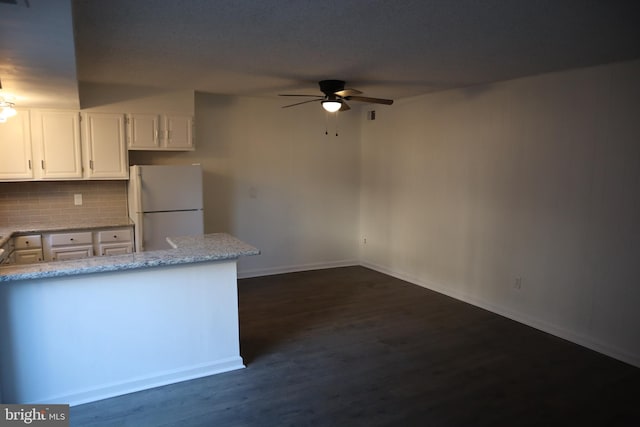 kitchen featuring light stone countertops, dark wood-style flooring, freestanding refrigerator, decorative backsplash, and white cabinets