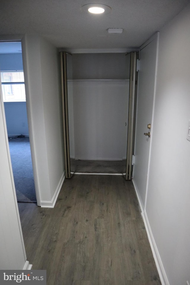 hall featuring a textured ceiling, baseboards, and wood finished floors