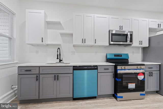 kitchen featuring light wood-type flooring, gray cabinets, stainless steel appliances, and a sink