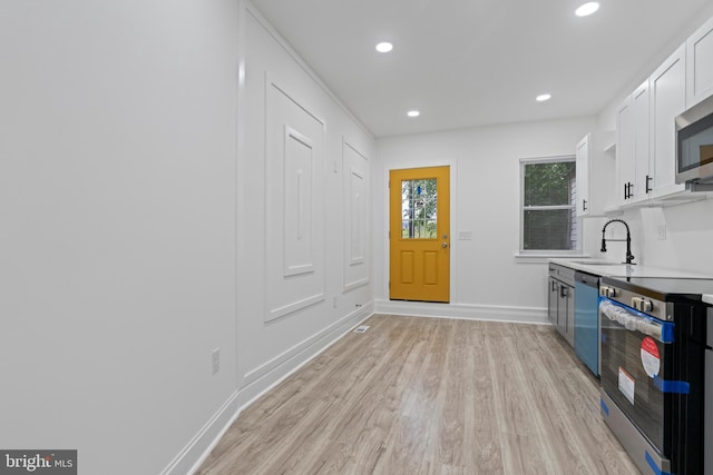 kitchen featuring recessed lighting, stainless steel appliances, a sink, white cabinets, and light wood-type flooring