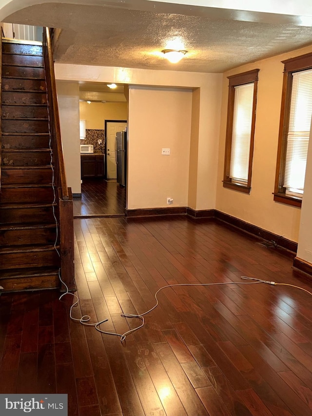 empty room with dark wood-style flooring, a textured ceiling, baseboards, and stairs