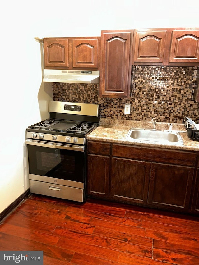 kitchen with under cabinet range hood, a sink, decorative backsplash, dark wood-style floors, and stainless steel range with gas stovetop