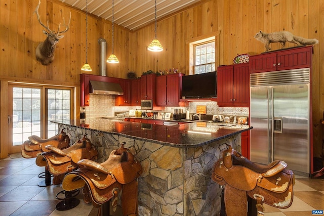 240 Stoneleigh Rd, Palmyra, VA 22963 - kitchen with built in refrigerator, wall chimney exhaust hood, reddish brown cabinets, backsplash, and wood walls