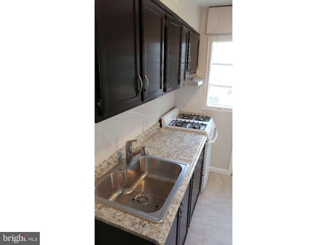 kitchen featuring light tile patterned floors, a sink, white range with gas cooktop, dark brown cabinets, and baseboards