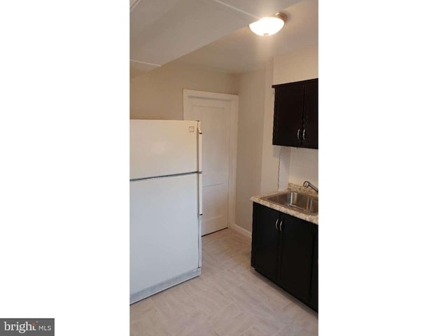 kitchen featuring dark cabinetry, light countertops, a sink, and freestanding refrigerator