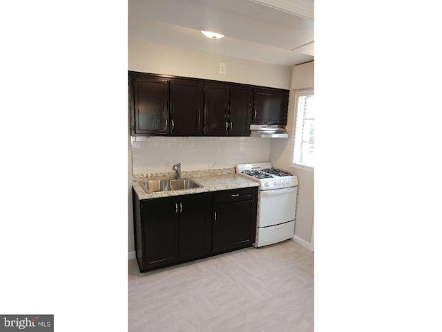 kitchen with decorative backsplash, range hood, white gas stove, and a sink