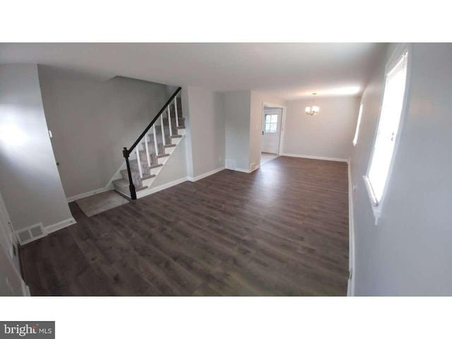 unfurnished living room with baseboards, visible vents, wood finished floors, stairs, and a notable chandelier