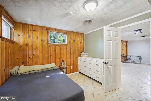 bedroom with light tile patterned floors, visible vents, a textured ceiling, and wood walls