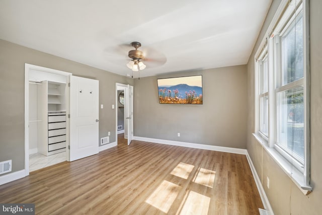 unfurnished bedroom featuring multiple windows, visible vents, a walk in closet, and wood finished floors