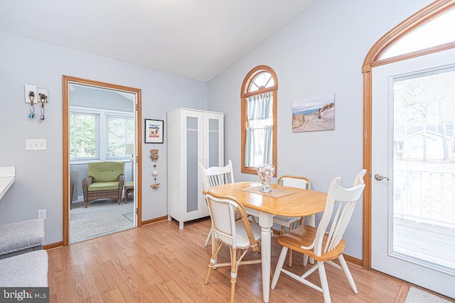 dining area featuring light wood-style flooring, baseboards, and vaulted ceiling