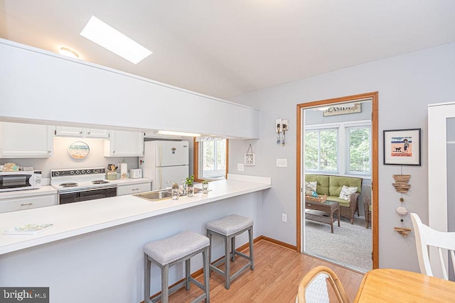 kitchen featuring a breakfast bar, light countertops, a skylight, white cabinets, and white appliances