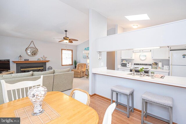 dining space with a glass covered fireplace, lofted ceiling with skylight, light wood-style floors, and a ceiling fan