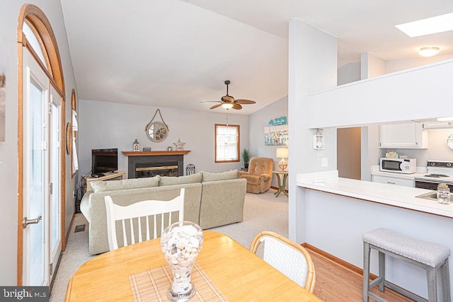 dining area with visible vents, lofted ceiling with skylight, light carpet, a glass covered fireplace, and ceiling fan